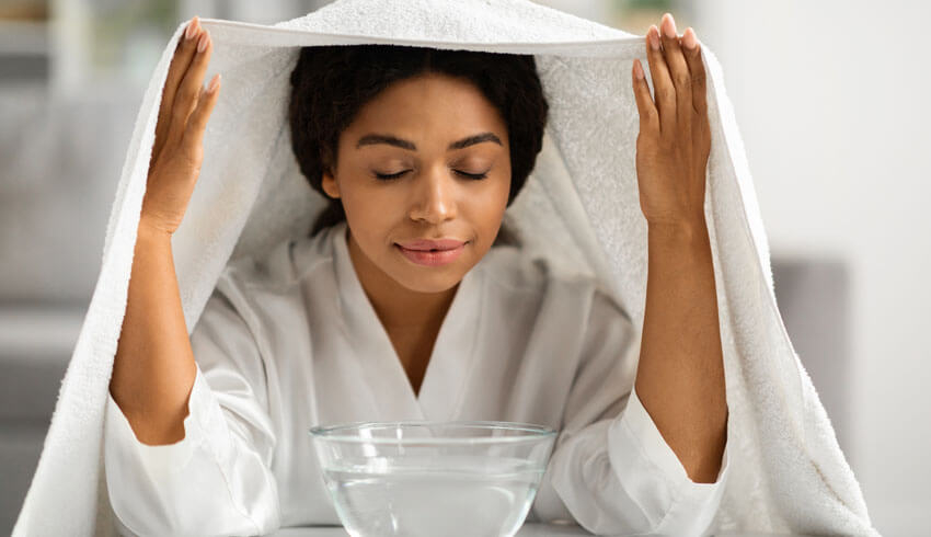 Woman steaming face over bowl of water with towel over head